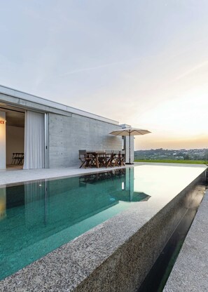 A modern building with a swimming pool, outdoor furniture, and a view of the landscape. - Alvarinho Villa — 5 Suites & Heated Pool (Amarante)