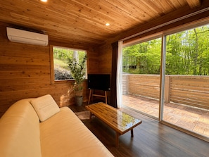 L’intérieur d’un chalet en bois, avec un canapé, un téléviseur et un balcon offrant une vue sur les arbres.