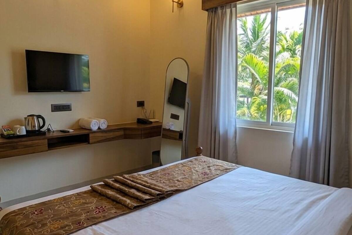 A hotel room with a large bed, a flat-screen TV, a bedside table with a lamp, and a window with curtains.