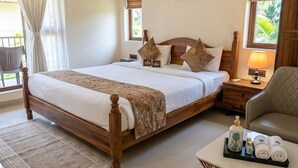 Un dormitorio con una cama grande, mesitas de noche, una silla, una mesita con artículos de aseo y una ventana con cortinas.