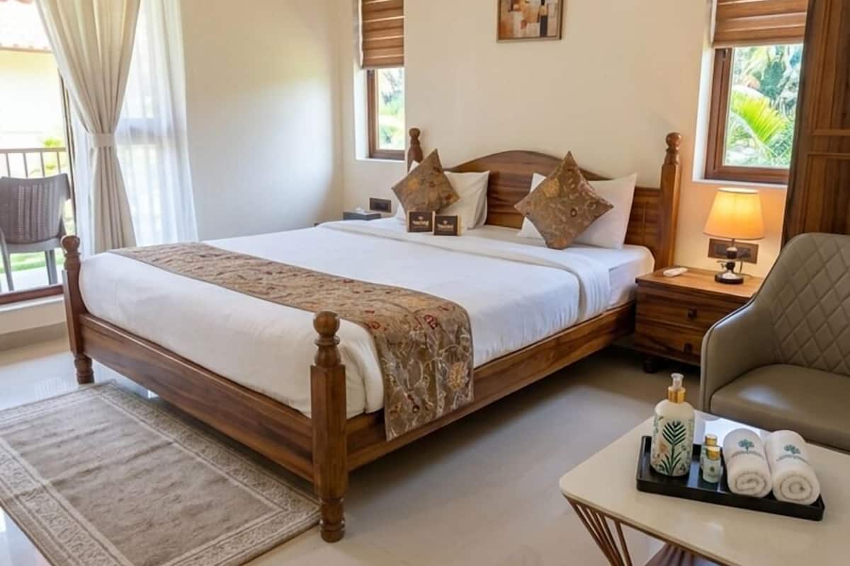 A bedroom with a large bed, bedside tables, a chair, a small table with toiletries, and a window with curtains.