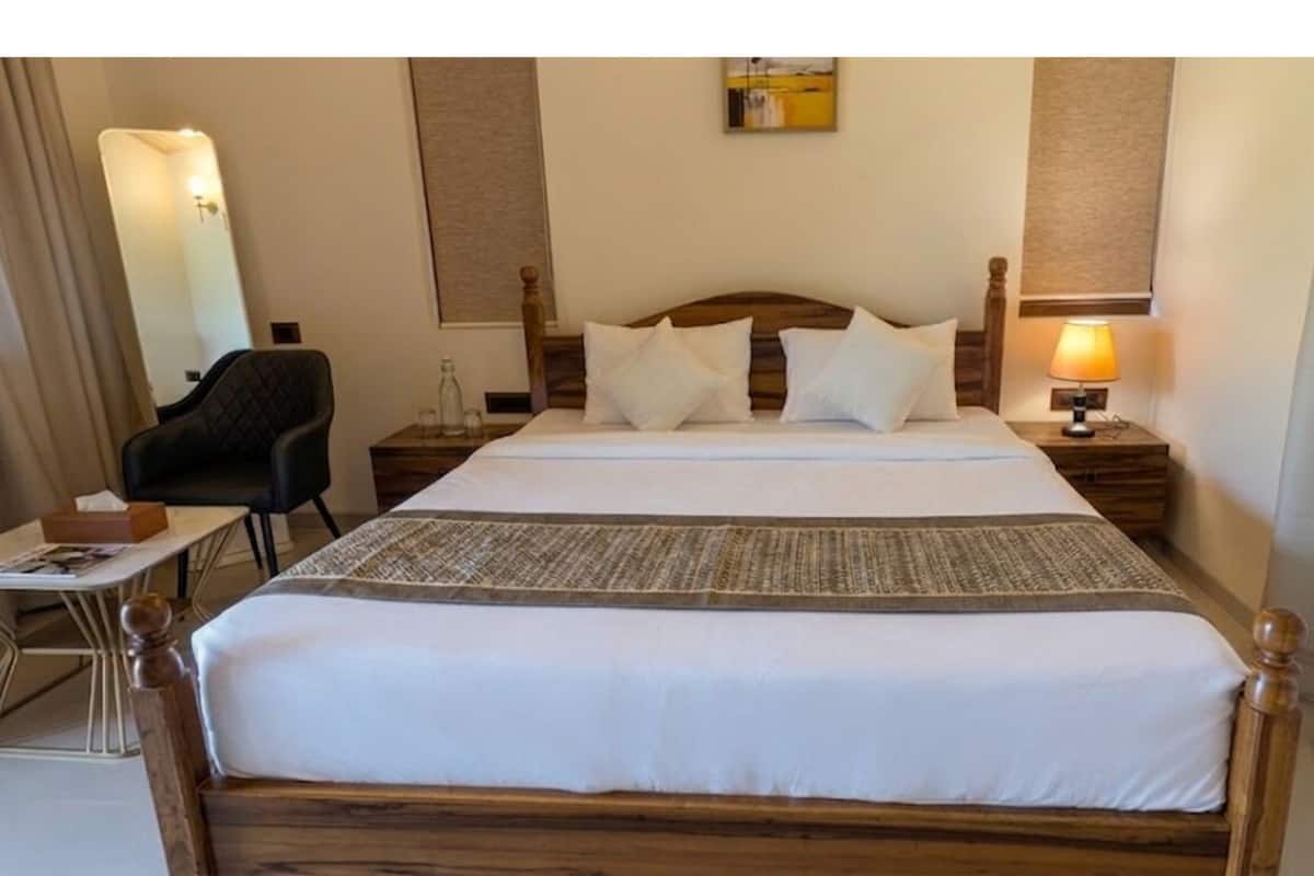 A hotel room with a wooden bed, a desk with a chair, a lamp, and a mirror.