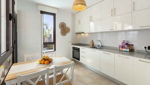 Une cuisine moderne avec des meubles blancs, une table en bois et un panier de fruits.