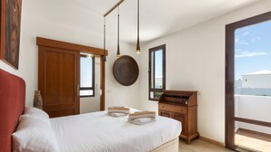 Une chambre à coucher avec un lit, une armoire en bois, un miroir rond et une fenêtre donnant sur un beau paysage.