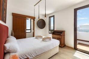 A bedroom with a bed, wooden wardrobe, a round mirror, and a window with a view. - Villa Bananagio - VipVipVillas (Playa Blanca)