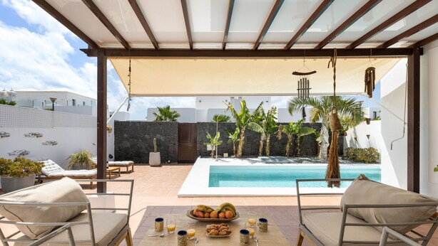 Un espace aménagé au bord de la piscine, avec une table dressée pour le petit-déjeuner, des chaises longues et une vue sur la piscine.