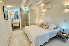 A bedroom with a bed, bedside table, nightstand, and a glass-enclosed shower. - Villa by the sea (Roquebrune-sur-Argens)