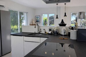 A modern kitchen with a central island, a built-in oven, and a large window providing a view of greenery. - Villa by the sea (Roquebrune-sur-Argens)