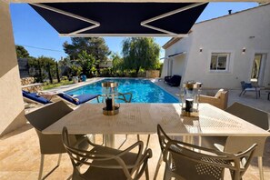 A poolside area with a table and chairs, a pool, and a covered seating area. - Villa by the sea (Roquebrune-sur-Argens)