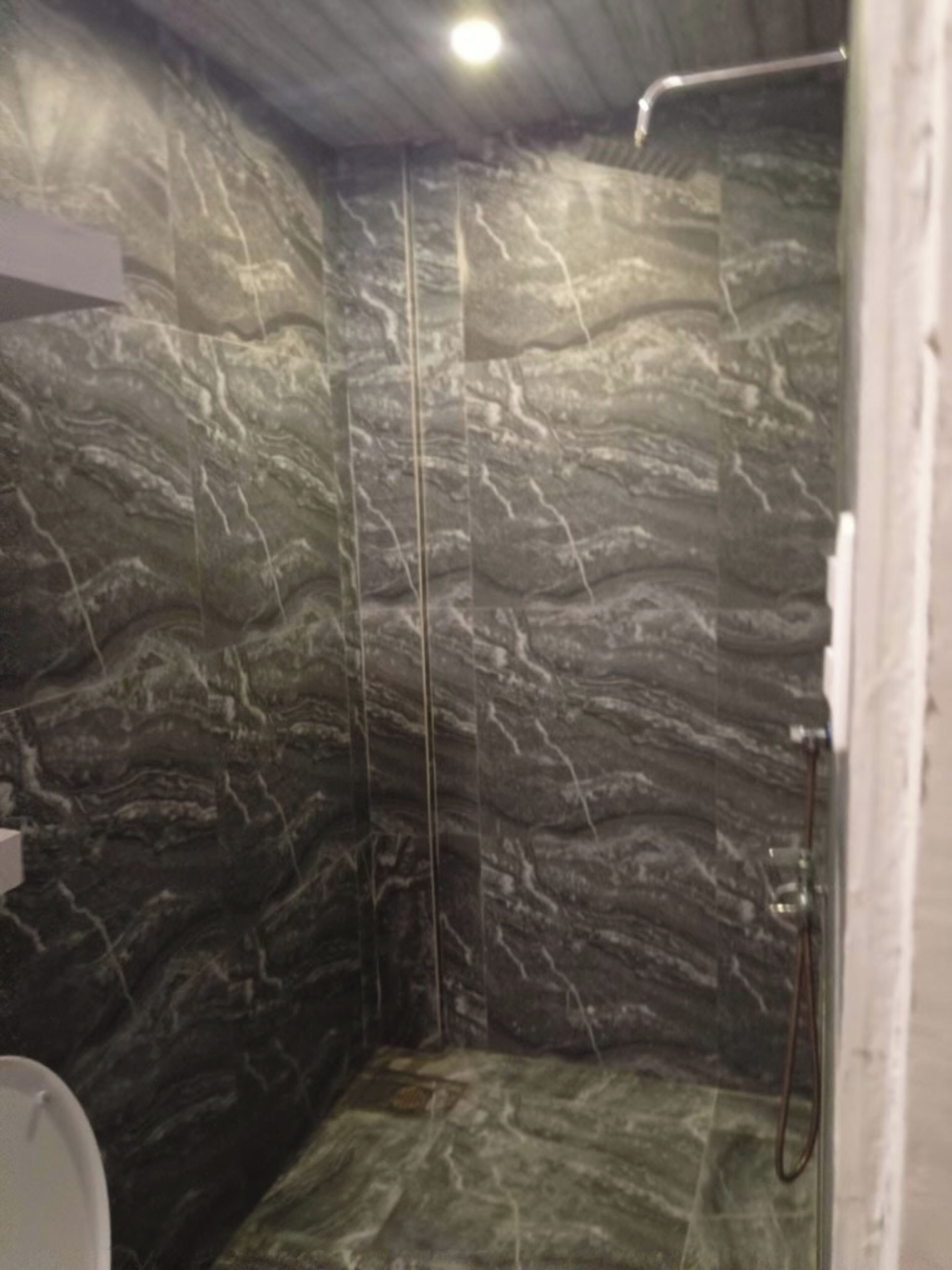 A bathroom with a shower, marble walls, and a white sink.