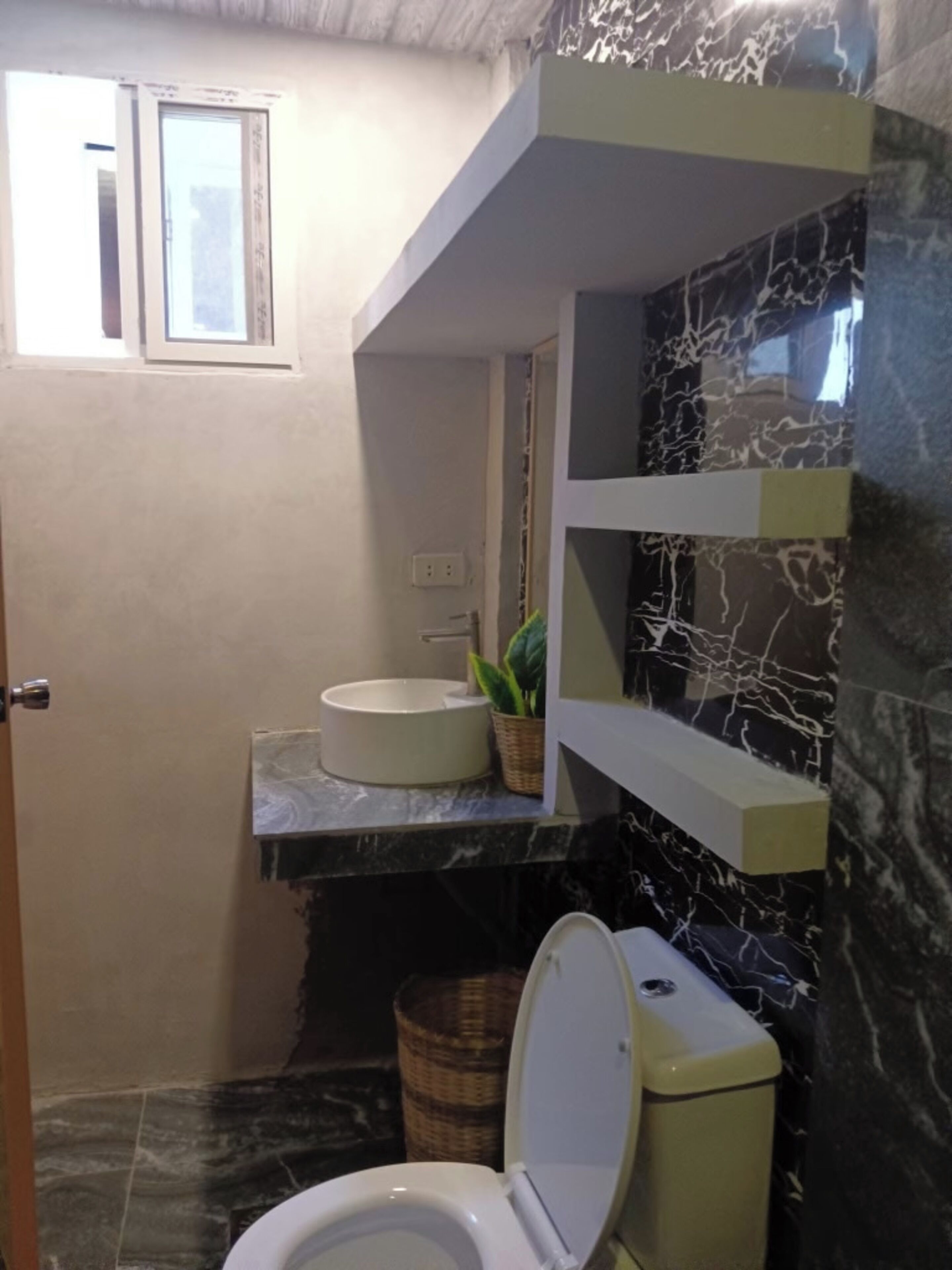 Un baño con inodoro, lavamanos y un ventanal pequeño.