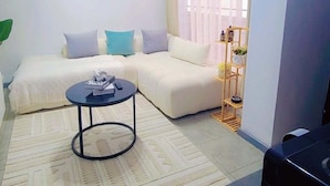 Una sala de estar con sofá, una mesa de centro, televisor y una ventana con cortinas.