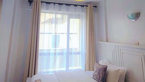Una habitación de hotel con una cama, cortinas, una ventana y una lámpara en el techo.