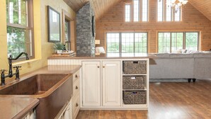 Une cuisine spacieuse dotée d’un grand îlot central, de poutres apparentes en bois au plafond et d’un mur d’accent en pierre.