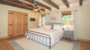 Une chambre à coucher comprenant un lit, des tables de chevet, un ventilateur de plafond, une porte en bois et une fenêtre avec des rideaux.