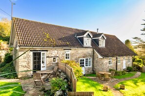 Ein Haus aus Stein mit Ziegeldach, Holzzaun und einer Terrasse mit Gartenmöbeln.