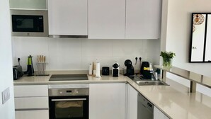 Une cuisine moderne avec des meubles blancs, des appareils électroménagers en acier inoxydable et un sol carrelé.