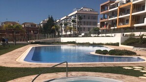 Un espace piscine avec un jacuzzi, entouré d’une terrasse en béton, et des immeubles d’habitation en arrière-plan.