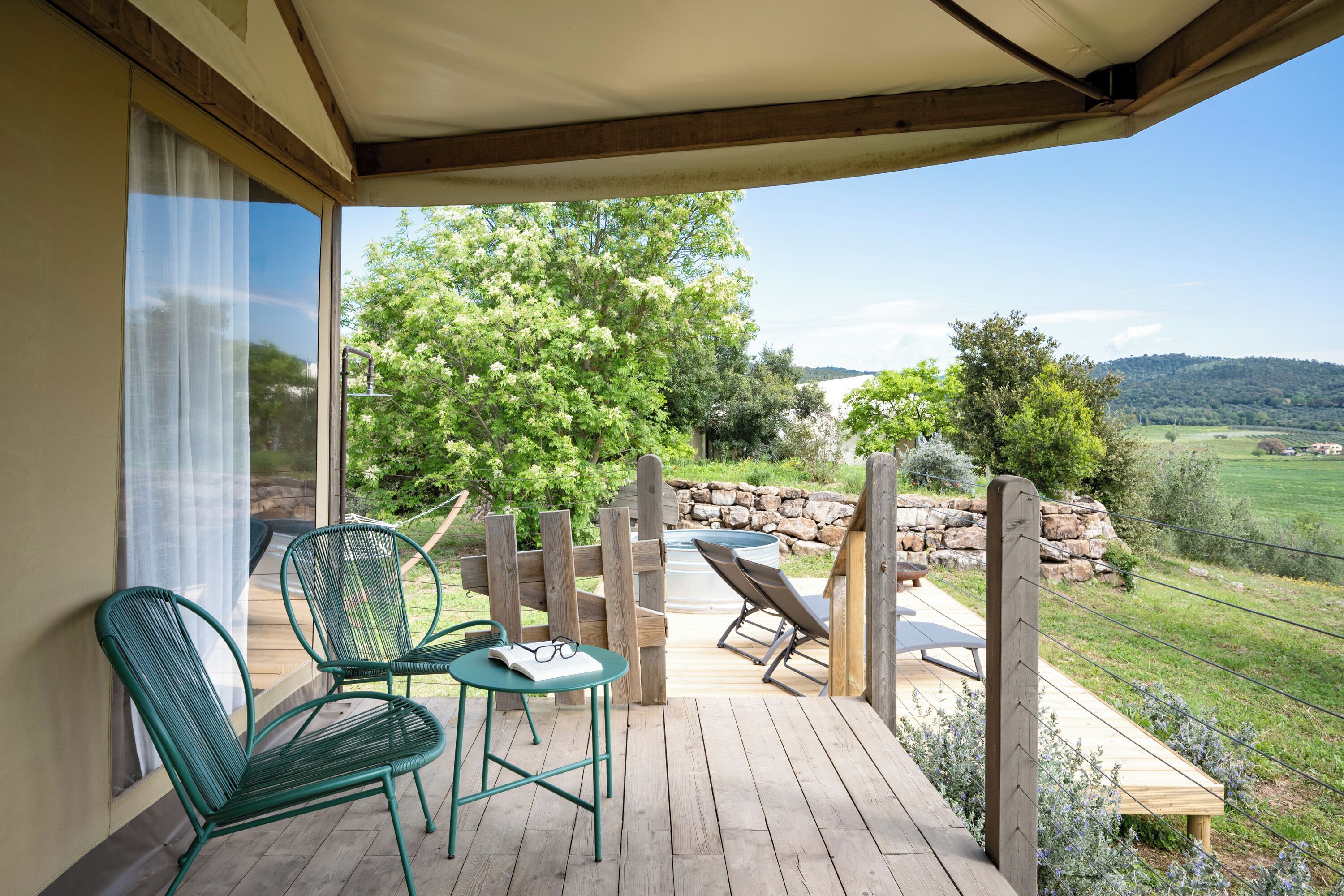A covered outdoor deck with chairs and a table, overlooking a garden and distant hills.