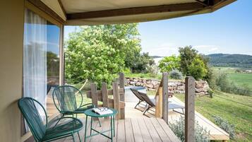 A covered outdoor deck with chairs and a table, overlooking a garden and distant hills.