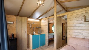 A wooden cabin interior with a kitchenette, a bed, and a sofa. - Glamping Stregaia (Massa Marittima)