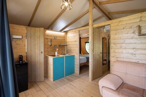 A wooden cabin interior with a kitchenette, a bed, and a sofa. - Glamping Stregaia (Massa Marittima)