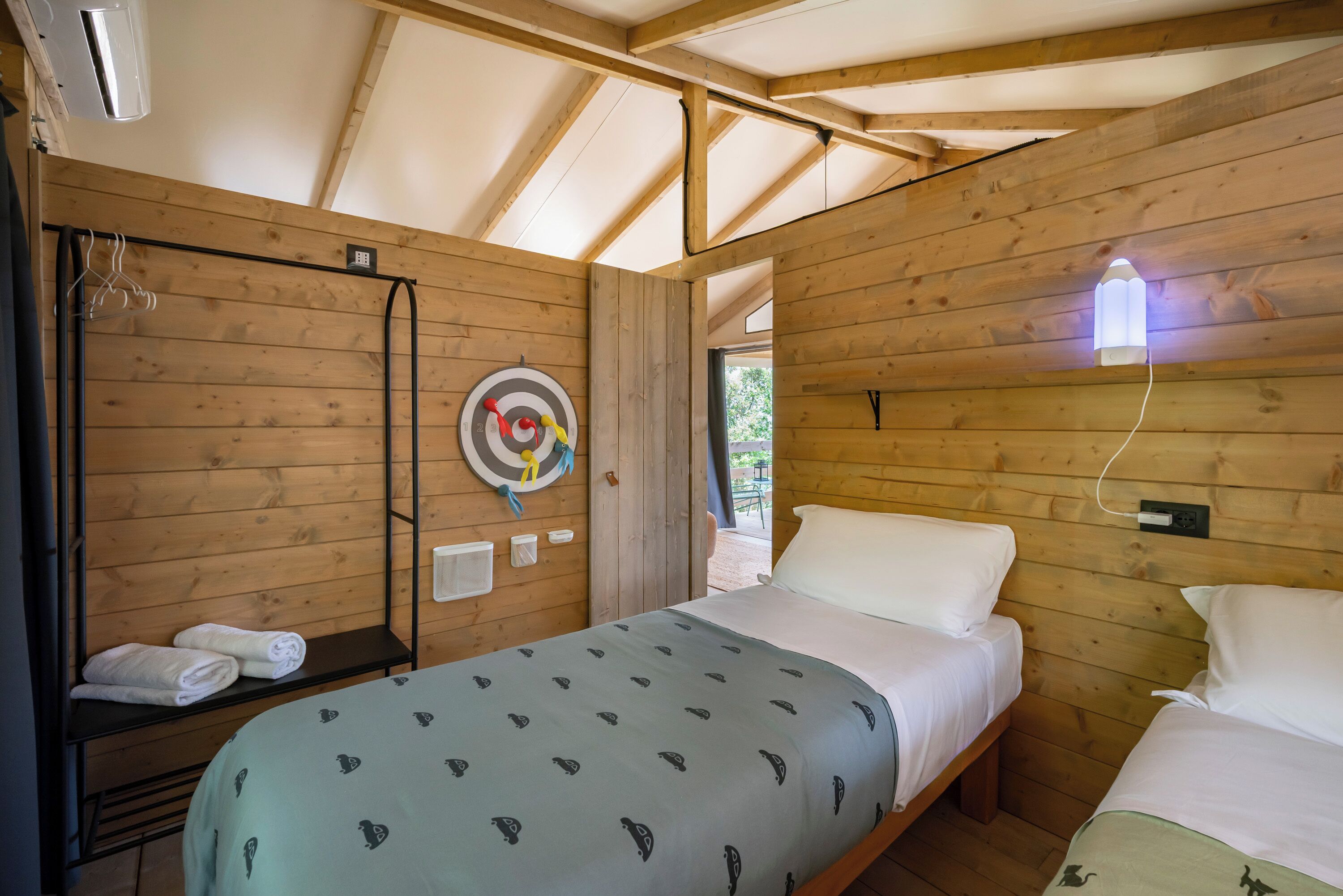 Una habitación tipo cabaña de madera con literas, un perchero y una ventana. Hay un blanco en la pared.