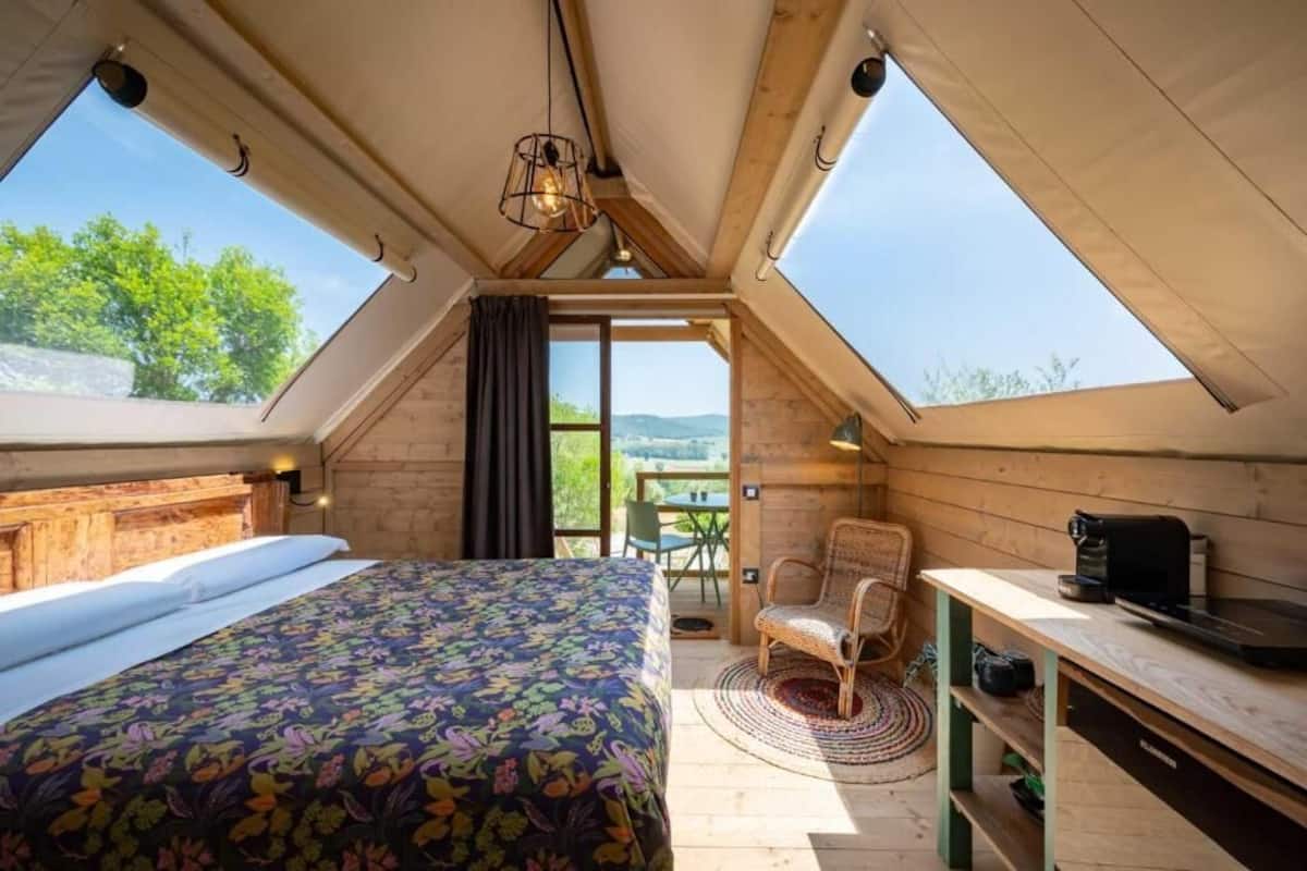 A bedroom with a bed, a desk, a chair, and a view of the outdoors.