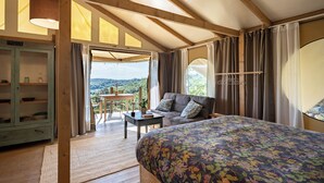 A bedroom with a bed, a sofa, a table, and a cabinet. There is a view of the outdoors through a window. - Glamping Stregaia (Massa Marittima)