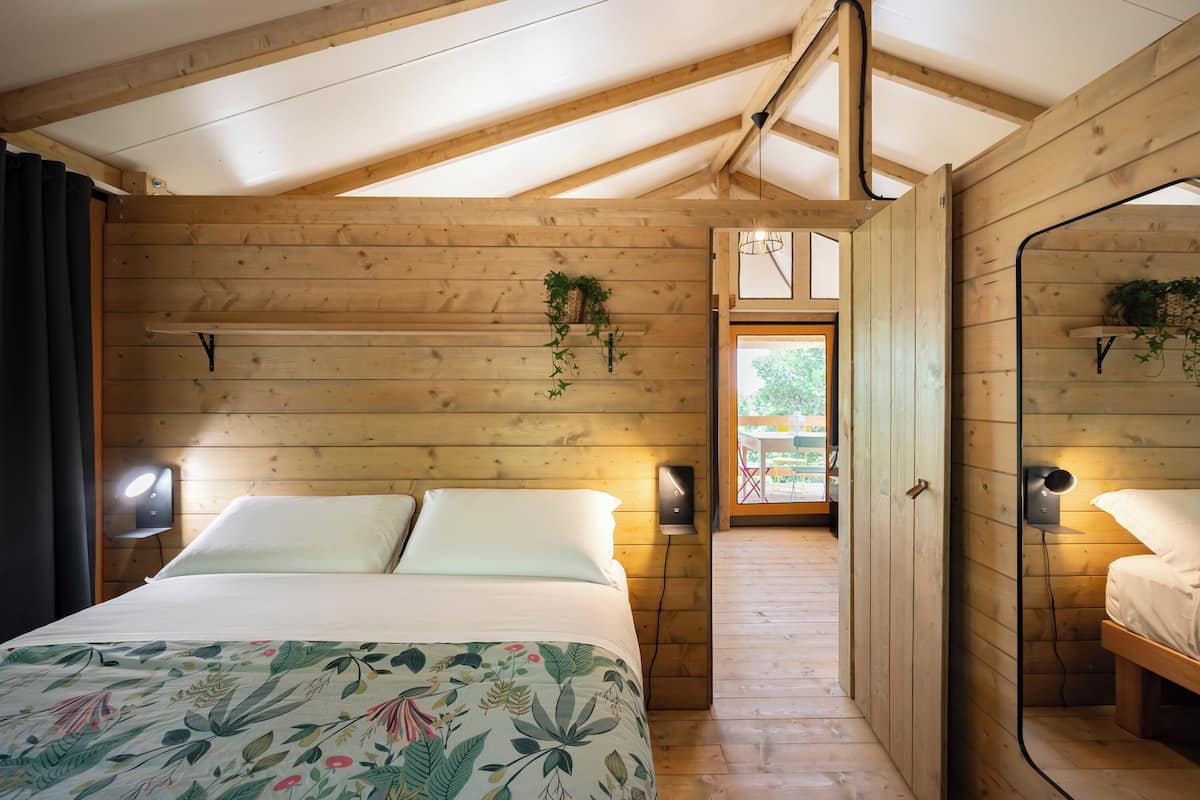 A wooden room with a bed, two wall-mounted lamps, and a hanging plant.