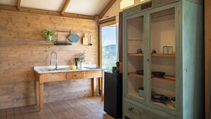 A wooden interior with a kitchen area, including a sink, a refrigerator, and a cabinet with glass doors. - Glamping Stregaia (Massa Marittima)