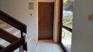 A staircase leading to a wooden door, a window with a view of buildings and trees, and a wall with a sign. - Familiar base for a comfortable stay in Rosolina (Rosolina Mare)