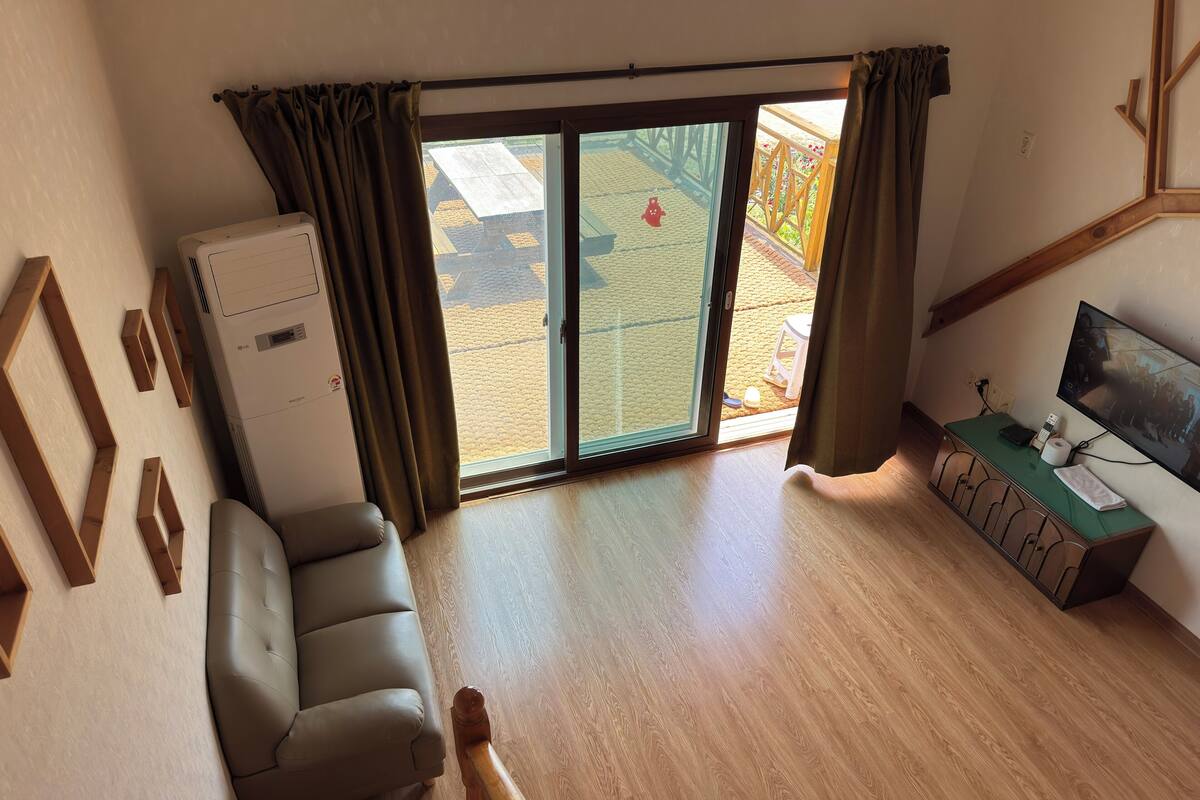 A living room with a sofa, a TV, a wooden cabinet, and a sliding glass door leading to an outdoor area.
