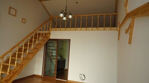 A wooden staircase leading to a loft area with a chandelier, a kitchen visible through a glass door, and a power outlet on the wall.