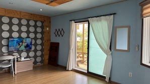 Una habitación con techo de madera, televisor en la pared, puerta corredera de vidrio y suelo de madera.