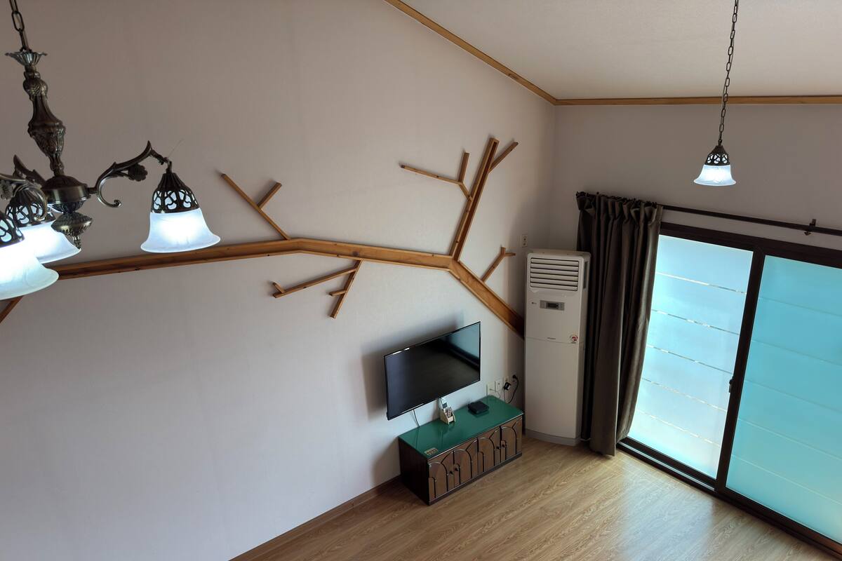 A room with a wooden ceiling, a flat-screen TV on a stand, an air conditioner, and a sliding glass door.