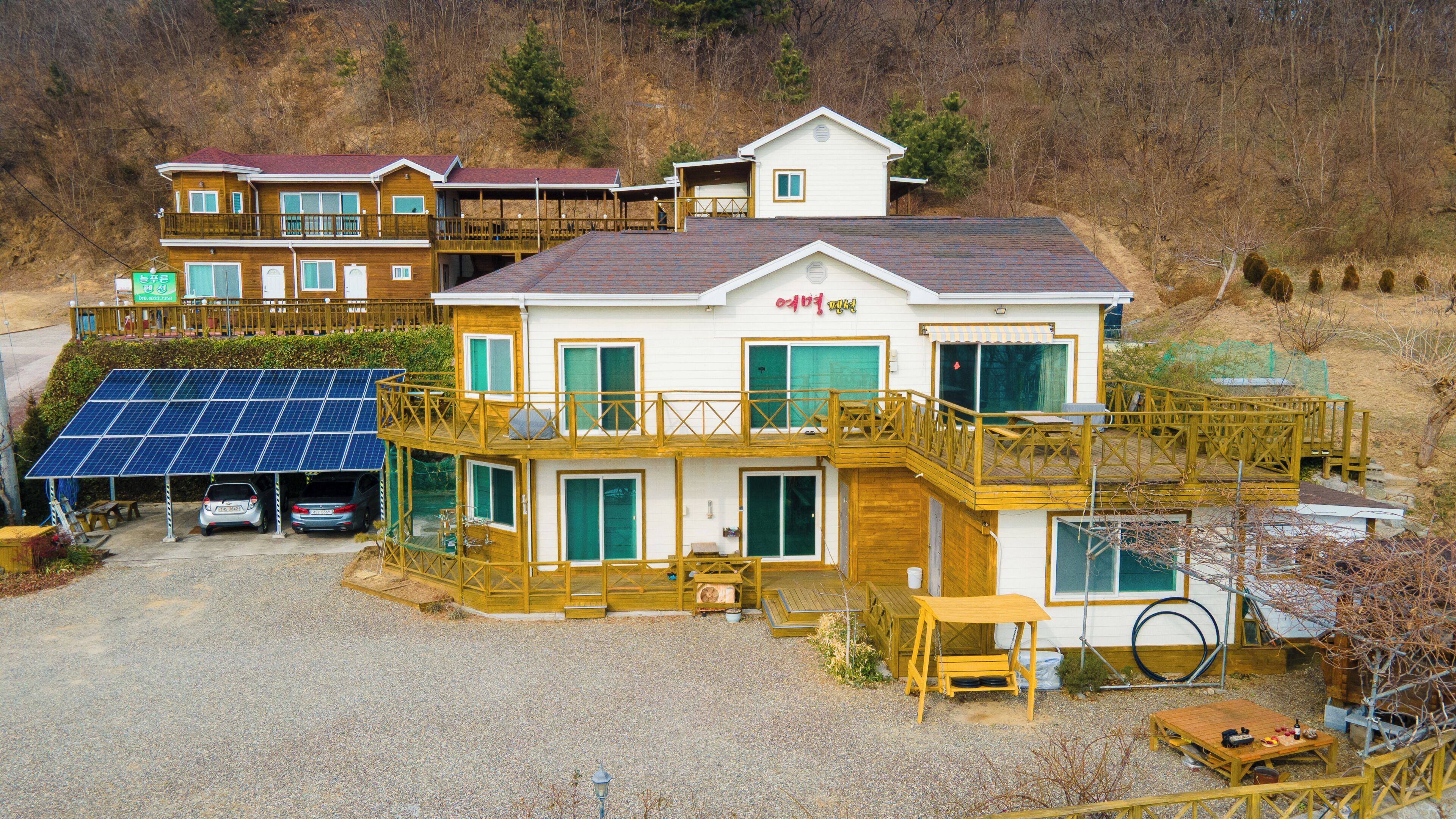 A multi-story house with a deck, solar panels, and a gravel driveway.