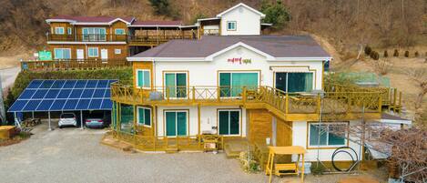 A multi-story house with a deck, solar panels, and a gravel driveway.
