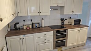 A kitchen with white cabinets, a wooden countertop, a coffee maker, a toaster, a microwave, and a built-in oven. - M4 Victoria Hub 5 (Newport)