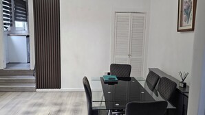 A modern dining area with a glass table, black chairs, a black sofa, a decorative light fixture, and a framed picture on the wall. - M4 Victoria Hub 5 (Newport)
