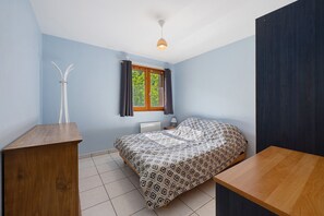 A bedroom with a bed, a wooden desk, a nightstand, a window with curtains, and a ceiling light. - "Bel Appartement Au Calme" with Balcony and Wi-Fi in Grand-Aigueblanche (Grand-Aigueblanche)