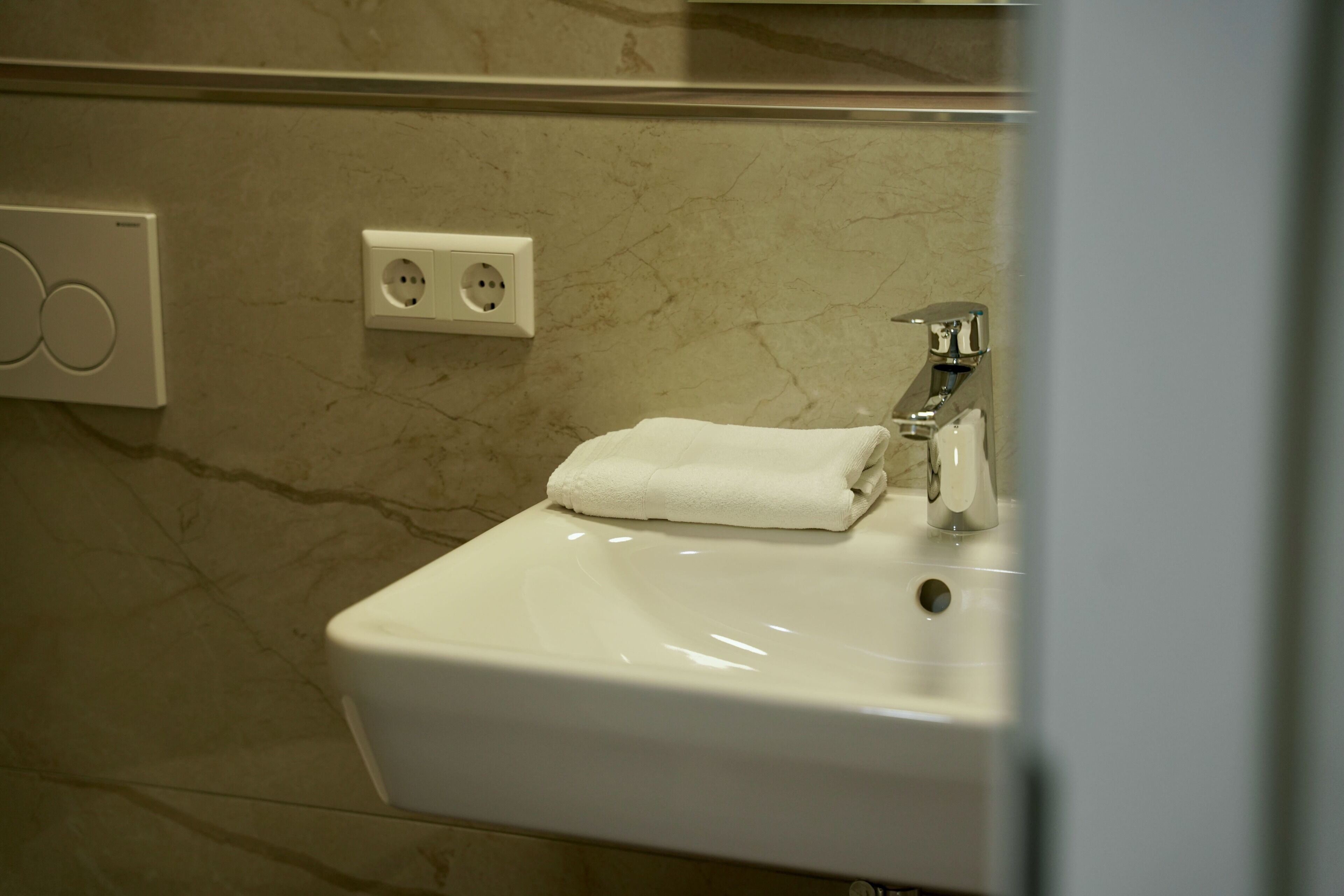 A bathroom with a white sink, a towel, a mirror, and a wall socket.