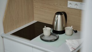 A kitchenette with a stainless steel kettle, two white cups with straws, a black induction cooktop, and a white countertop. - Mersa Hotel (Backnang)
