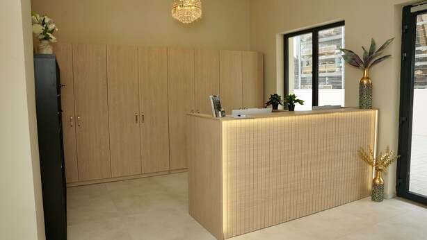 A reception desk with a wooden panel design, a chandelier, and potted plants. - Mersa Hotel (Backnang)