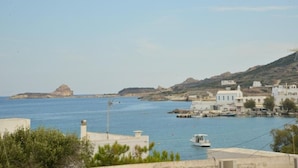 A coastal town with buildings, a boat, and a rocky island in the distance. - Studios Kymata  (Milos)