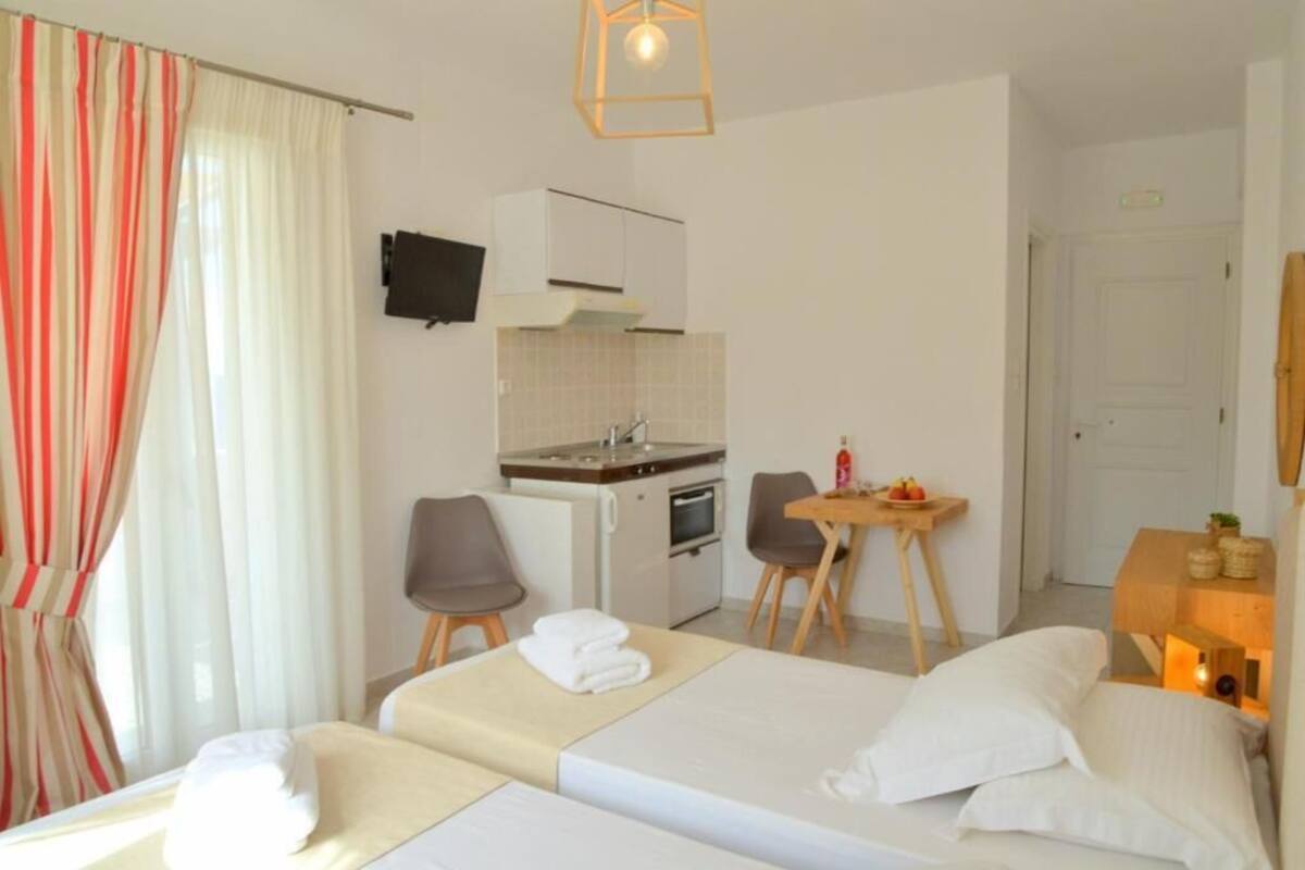 A hotel room with a bed, a desk, a chair, a small kitchenette, and a TV on the wall.