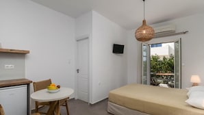 A compact room with a bed, a small table with fruit, a TV, and a window with an outdoor view. - Studios Kymata  (Milos)