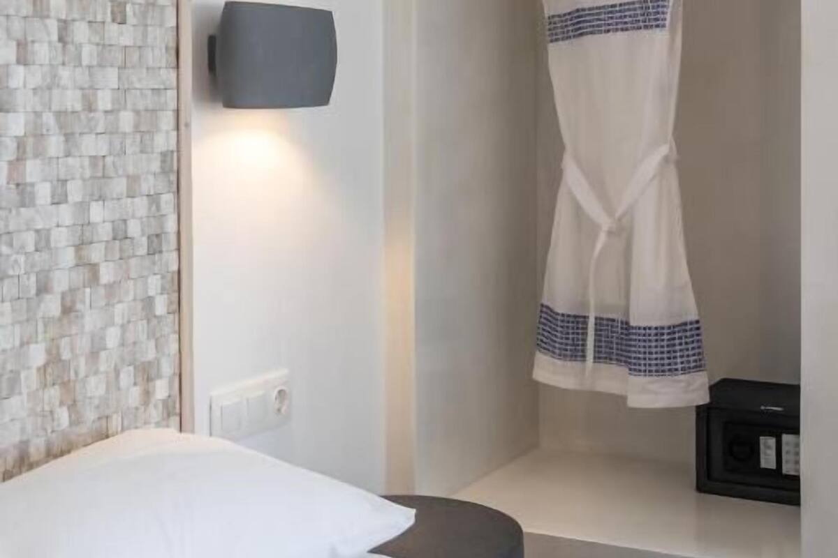 A hotel room with a bed, a wall-mounted light, a wardrobe, and a hanging garment.