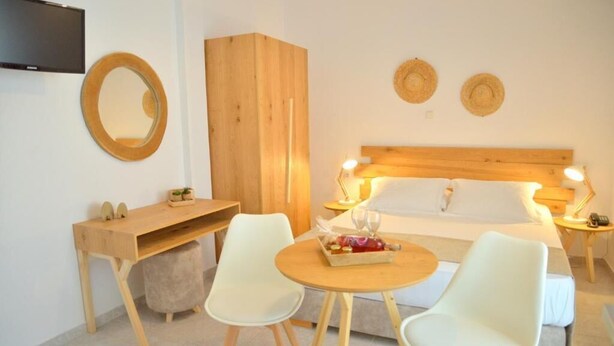 A bedroom with a bed, bedside tables, a desk, two chairs, a TV, and a wall-mounted mirror. - Studios Kymata  (Milos)