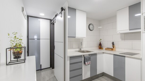 Une cuisine moderne avec des meubles blancs, un évier, une horloge et une plante en pot.